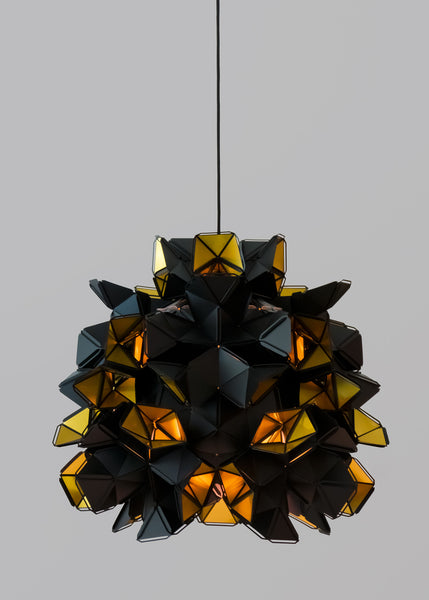 The Labyrinth Lamp is a light sculpture by Republiken.  Featured in this image with an open bottom to let light flood out. The outside of the Labyrinth light sculpture has a matte black surface which contrast the protruding openings where the reflective inside is exposed.